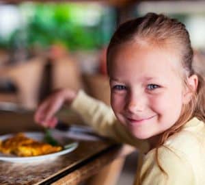 Casual portrait of adorable little girl enjoying meal at restaurant